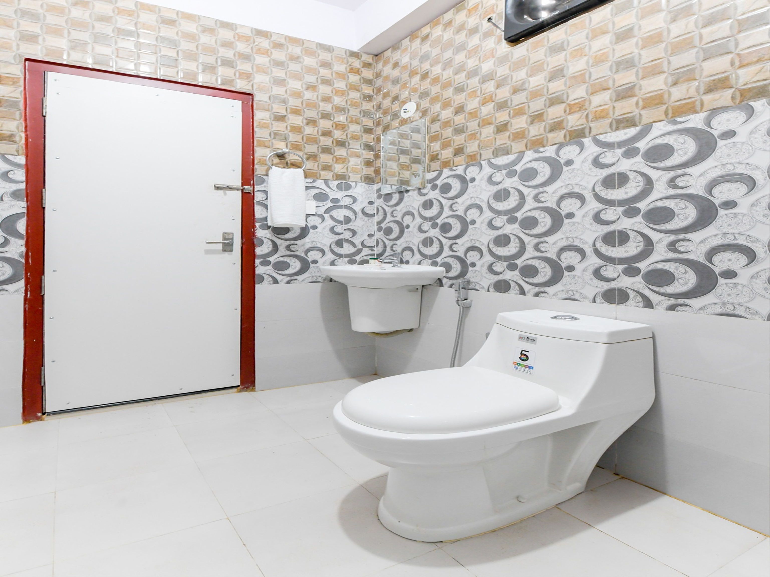 A bathroom with a white toilet, a sink, and a door. The walls have a patterned tile design.