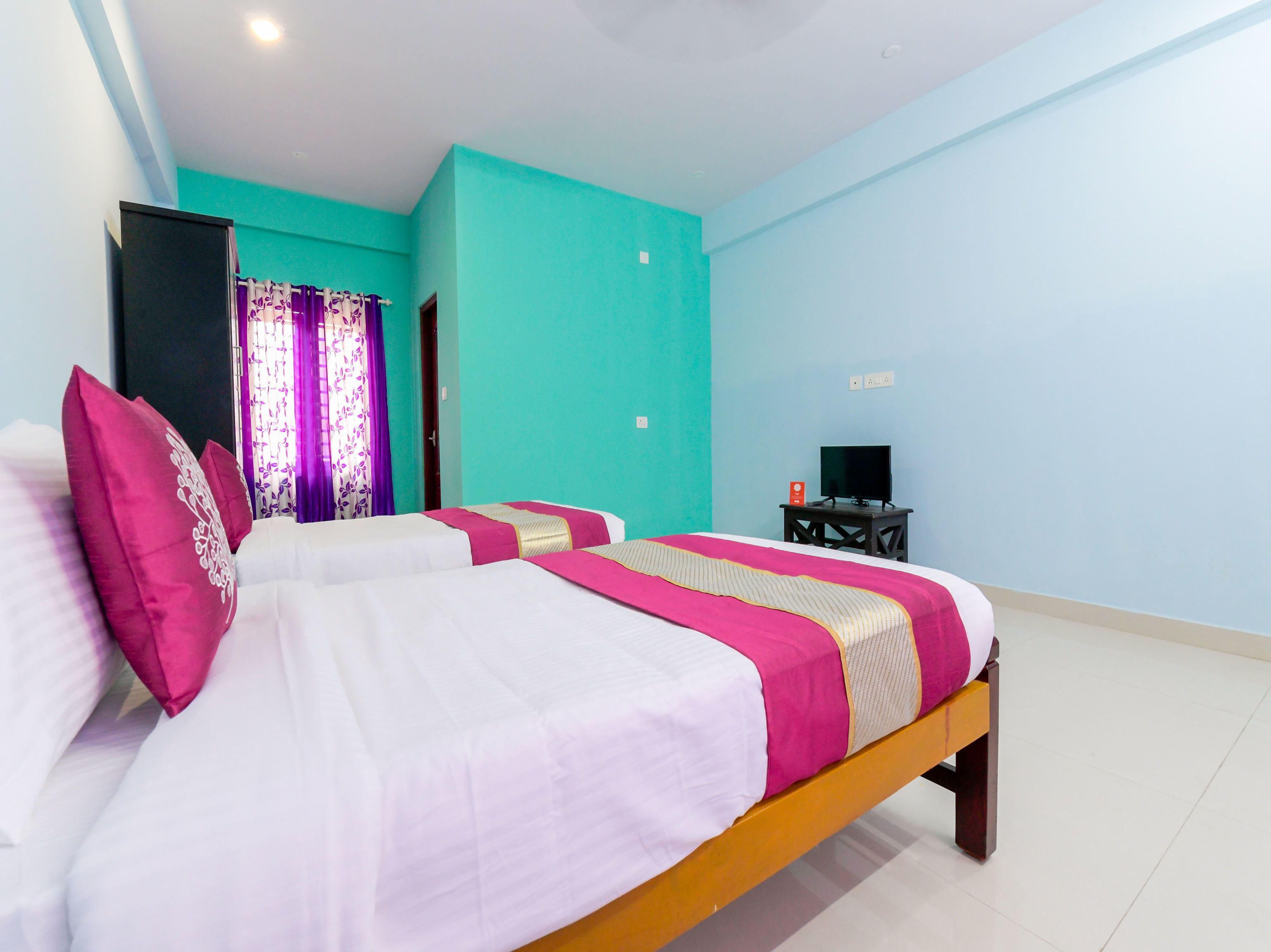 Une chambre d’hôtel avec deux lits, un téléviseur posé sur une petite table et un mur de couleur turquoise.