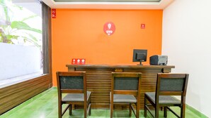 Un comptoir d’accueil avec un revêtement en bois, un écran d’ordinateur et un téléphone. Il y a trois chaises devant le comptoir. Le mur derrière le comptoir est de couleur orange.