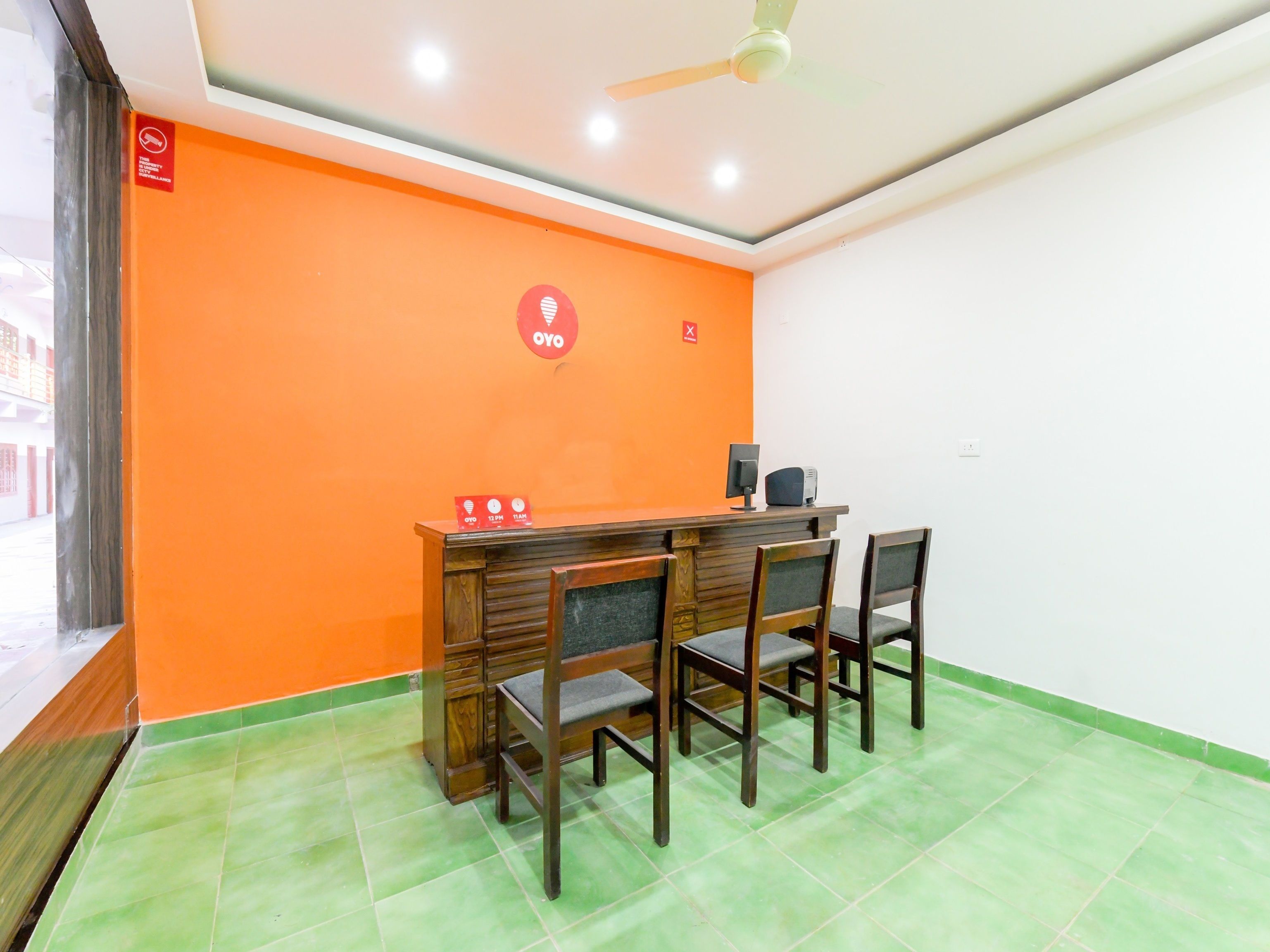 Un salón de conferencias con una pared naranja, un escritorio de madera con una computadora y un altavoz, y cuatro sillas.