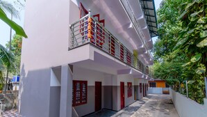 Un bâtiment à deux étages doté d’une cour dallée, de portes rouges et d’un balcon orné d’une rambarde en métal.