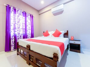 A neatly arranged bedroom with a wooden bed, a nightstand, and an air conditioning unit on the wall. - OYO 11620 Amare Highway Residency (Ambalapuzha)