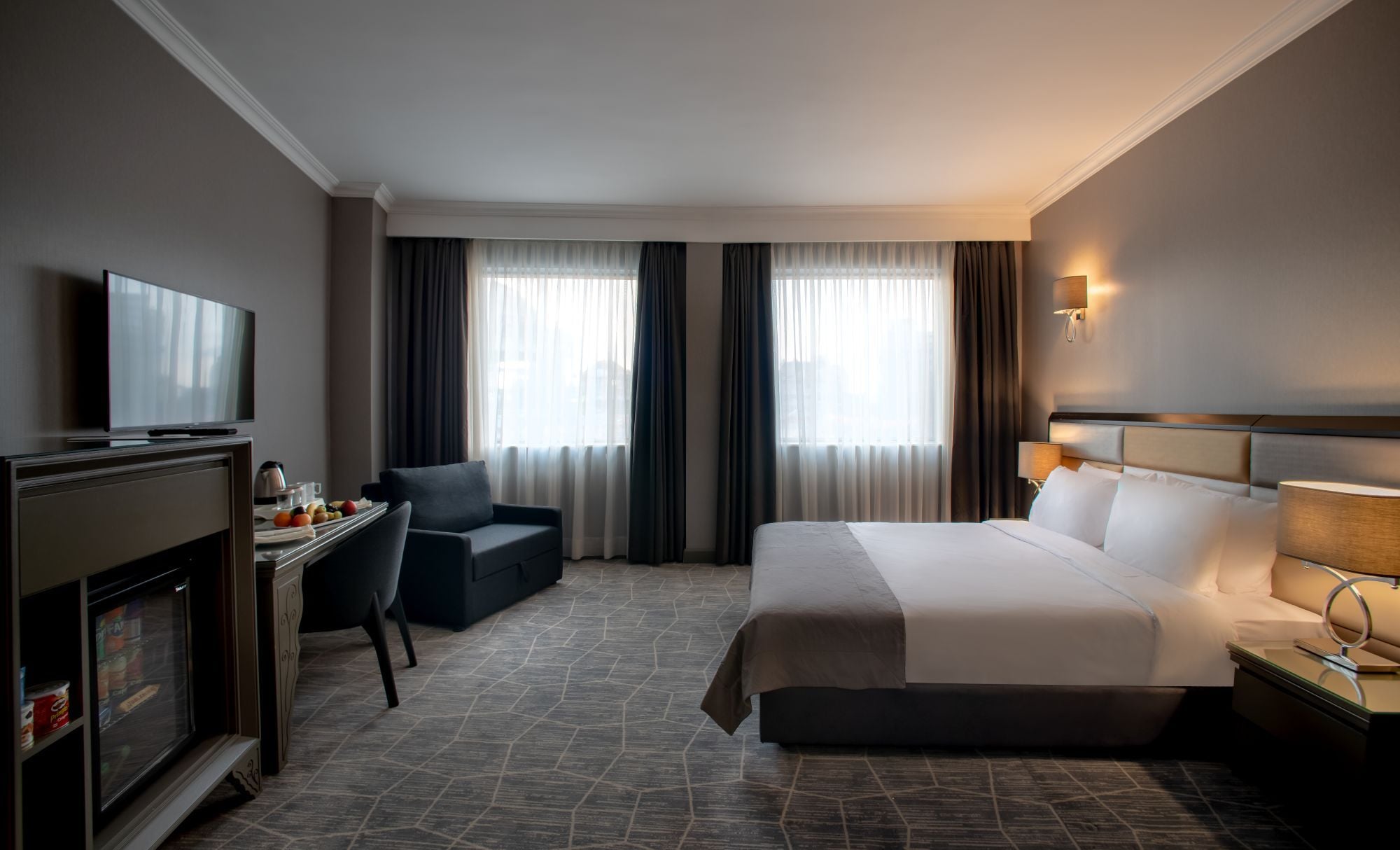 Ein Hotelzimmer mit einem Bett, einem Schreibtisch mit Fernseher, einem Sessel und einer Minibar.