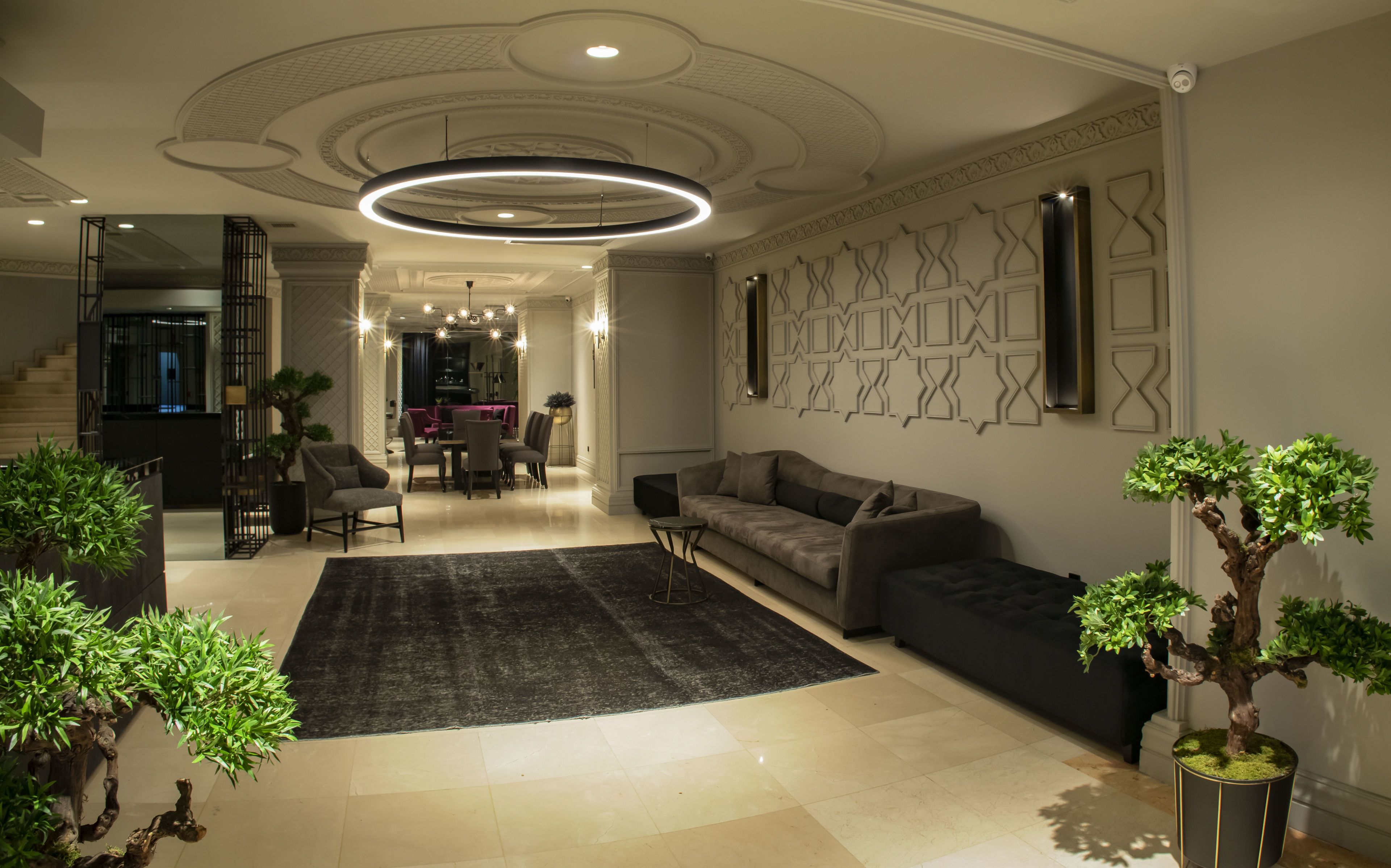 A modern living room with a sofa, a coffee table, and a rug. There are two potted plants and a staircase leading to another room.