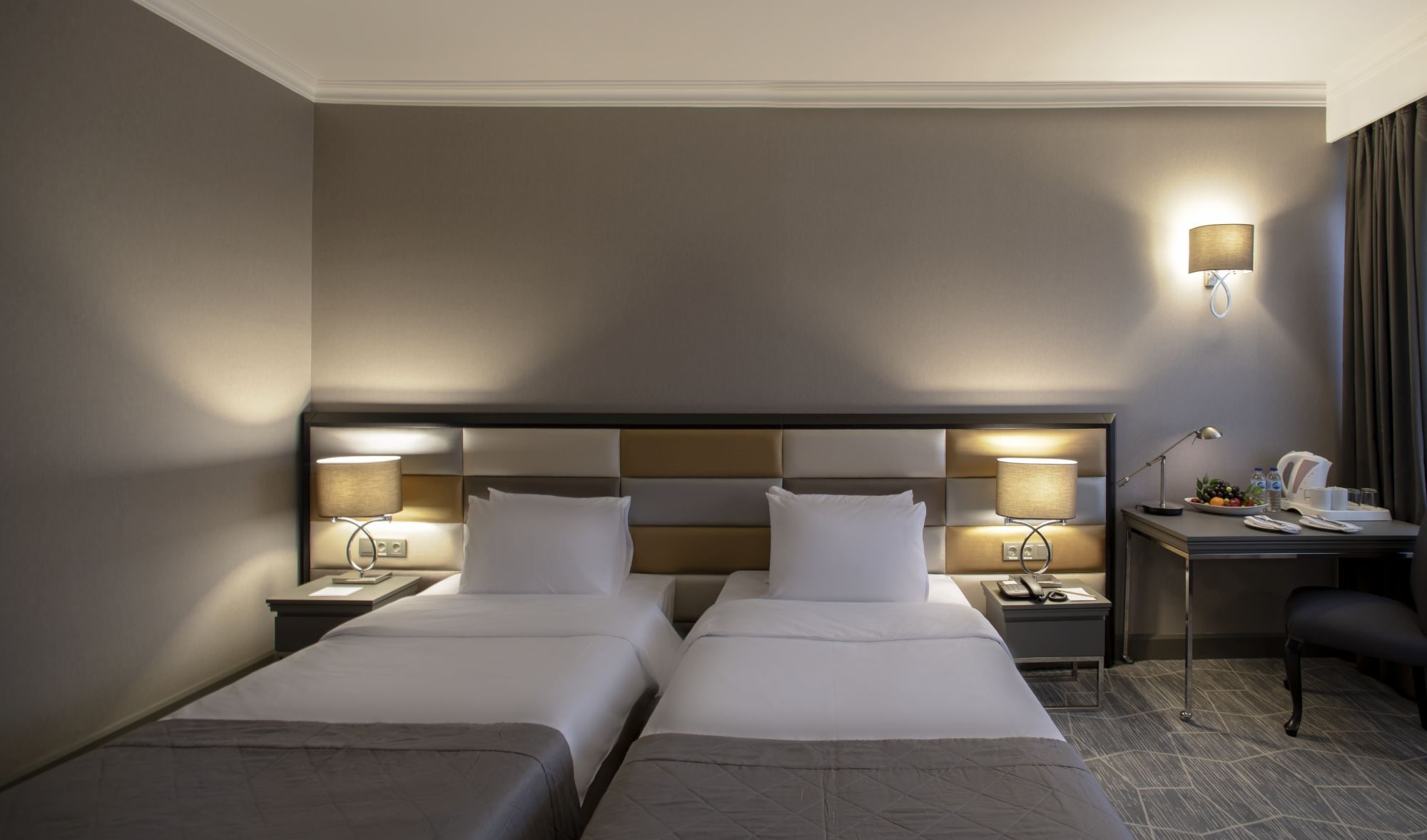A hotel room with two beds, a desk, a chair, and a nightstand with lamps.