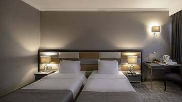 A hotel room with two beds, a desk, a chair, and a nightstand with lamps.
