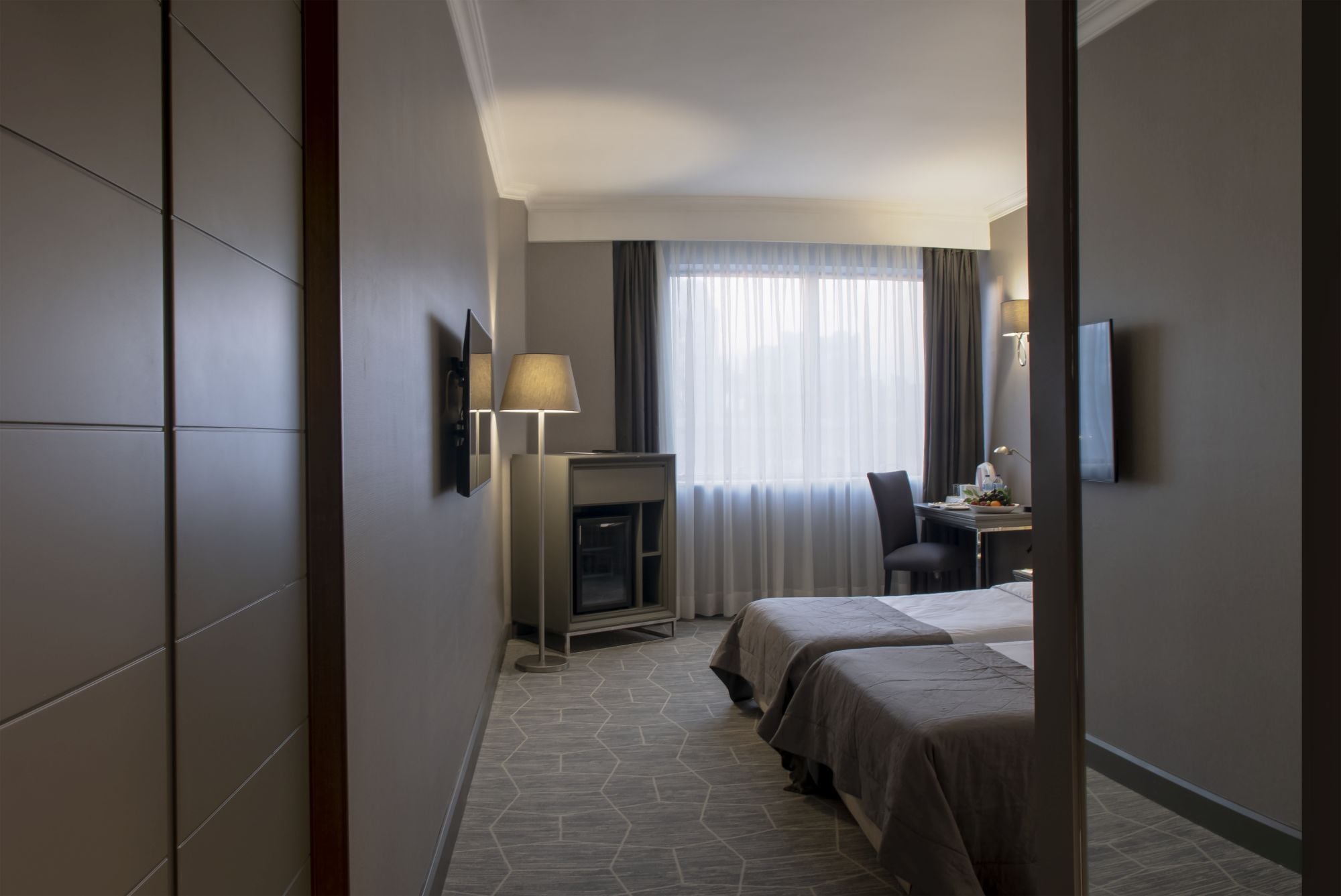 Une chambre d’hôtel avec une cheminée, un bureau avec une lampe, deux lits et un téléviseur fixé au mur.
