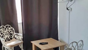 A room with two white ornate chairs, a small wooden table, a remote control on the table, and a TV mounted on the wall. - Bono Beach Hotel (Odesa)