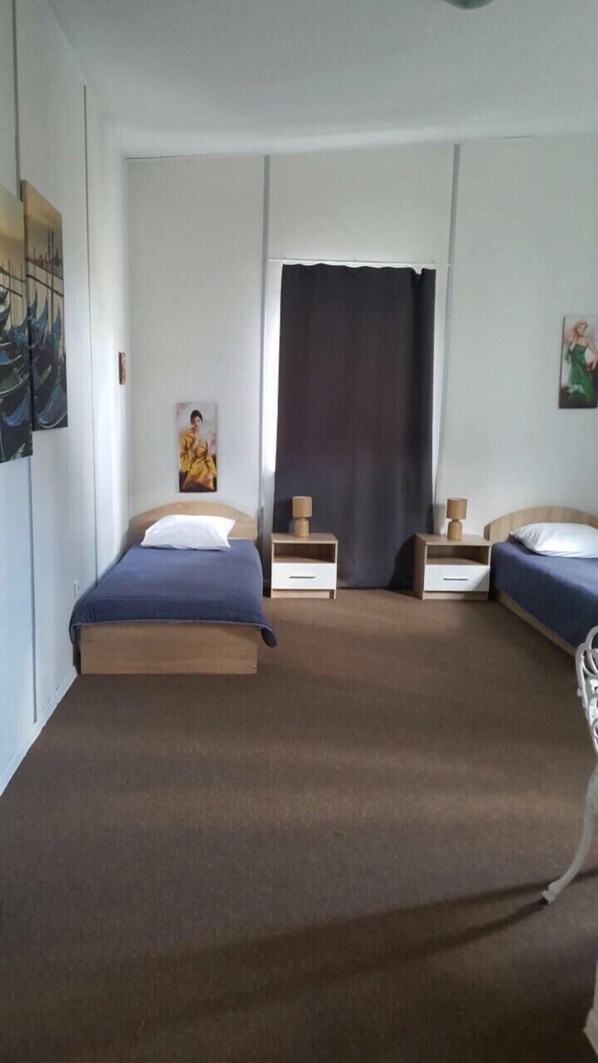 A bedroom with two single beds, a large window with a dark curtain, and a painting on the wall.