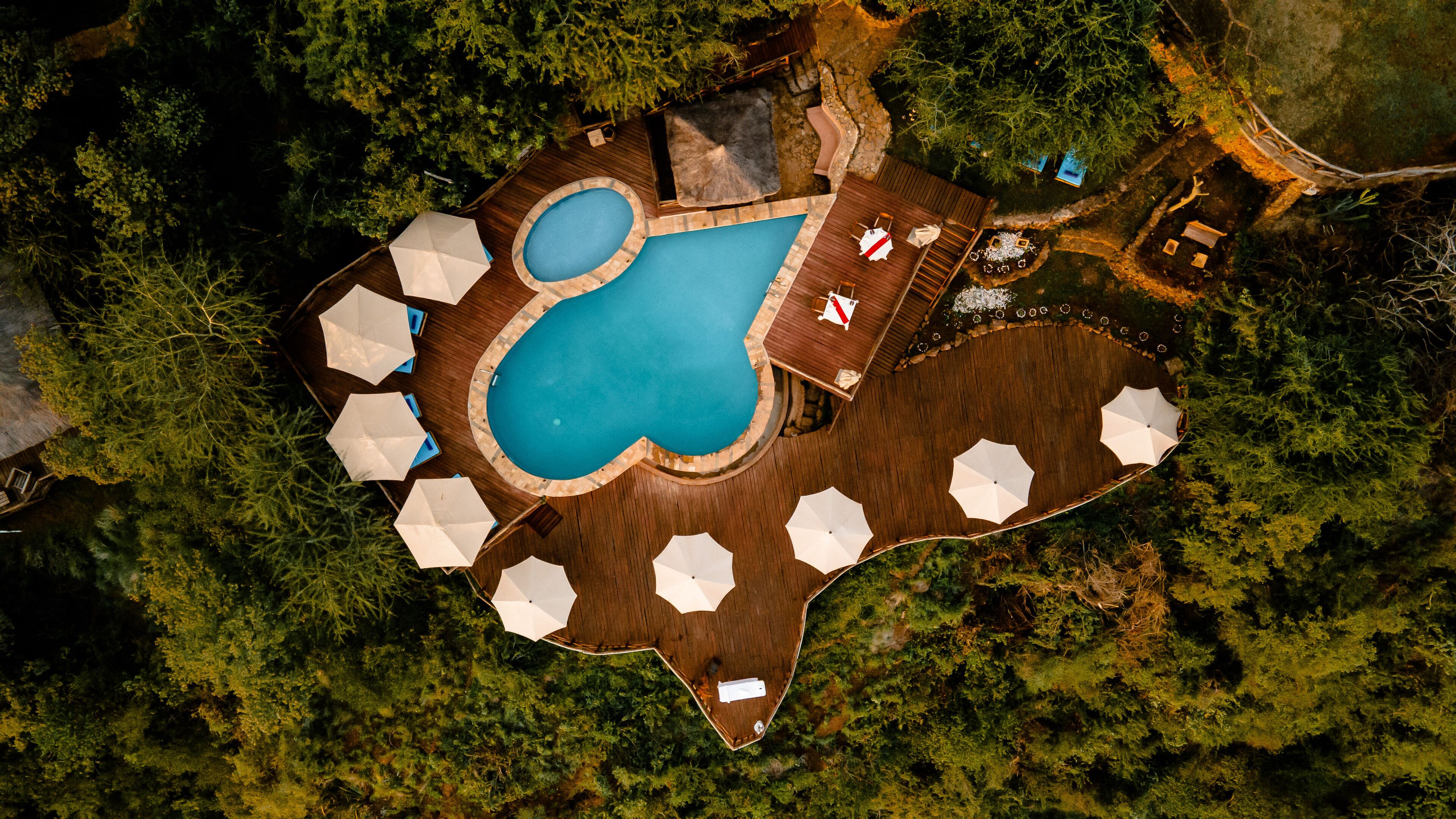 Vista aèria d'una zona de piscina amb una piscina circular, envoltada per un terra de fusta i paraigües blancs.