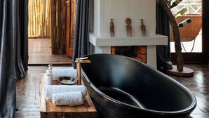Een moderne badkamer met een vrijstaand bad, een houten bankje en een decoratieve wandversiering.