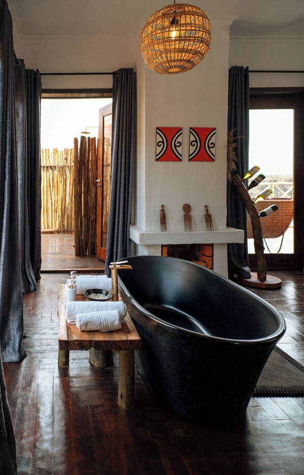 A modern bathroom with a freestanding bathtub, wooden bench, and a decorative wall piece. - Escarpment Luxury Lodge (Lake Manyara National Park)