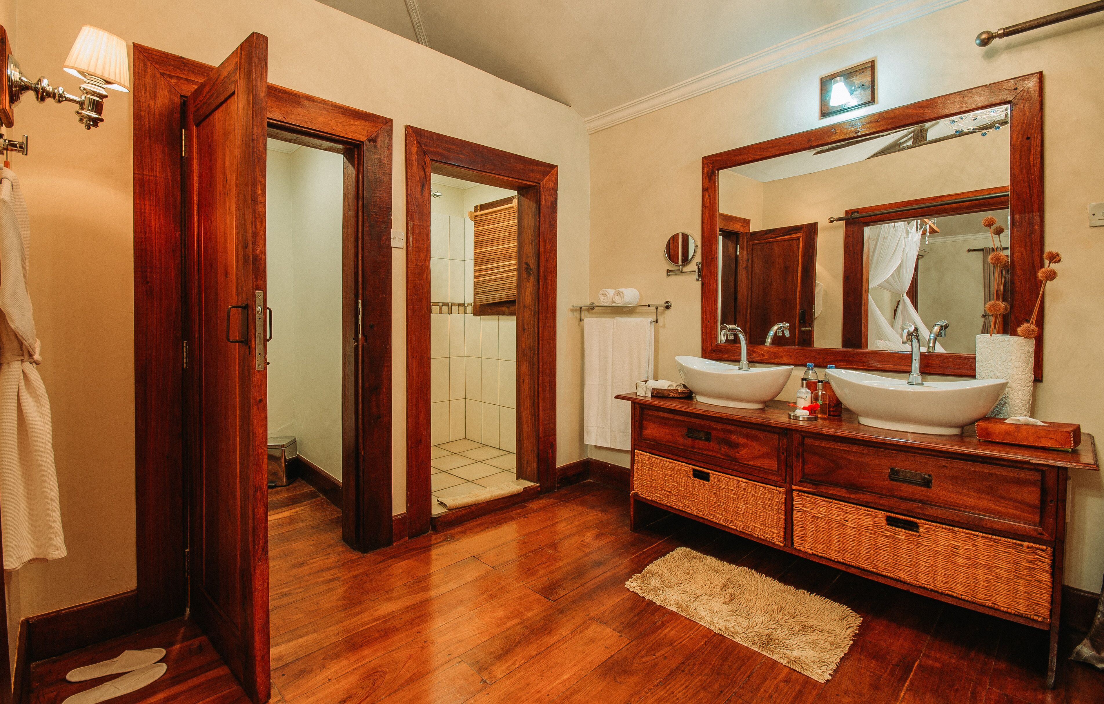 Ein Badezimmer mit Holzboden, einem großen Spiegel, zwei Waschbecken und einer Holzkommode.