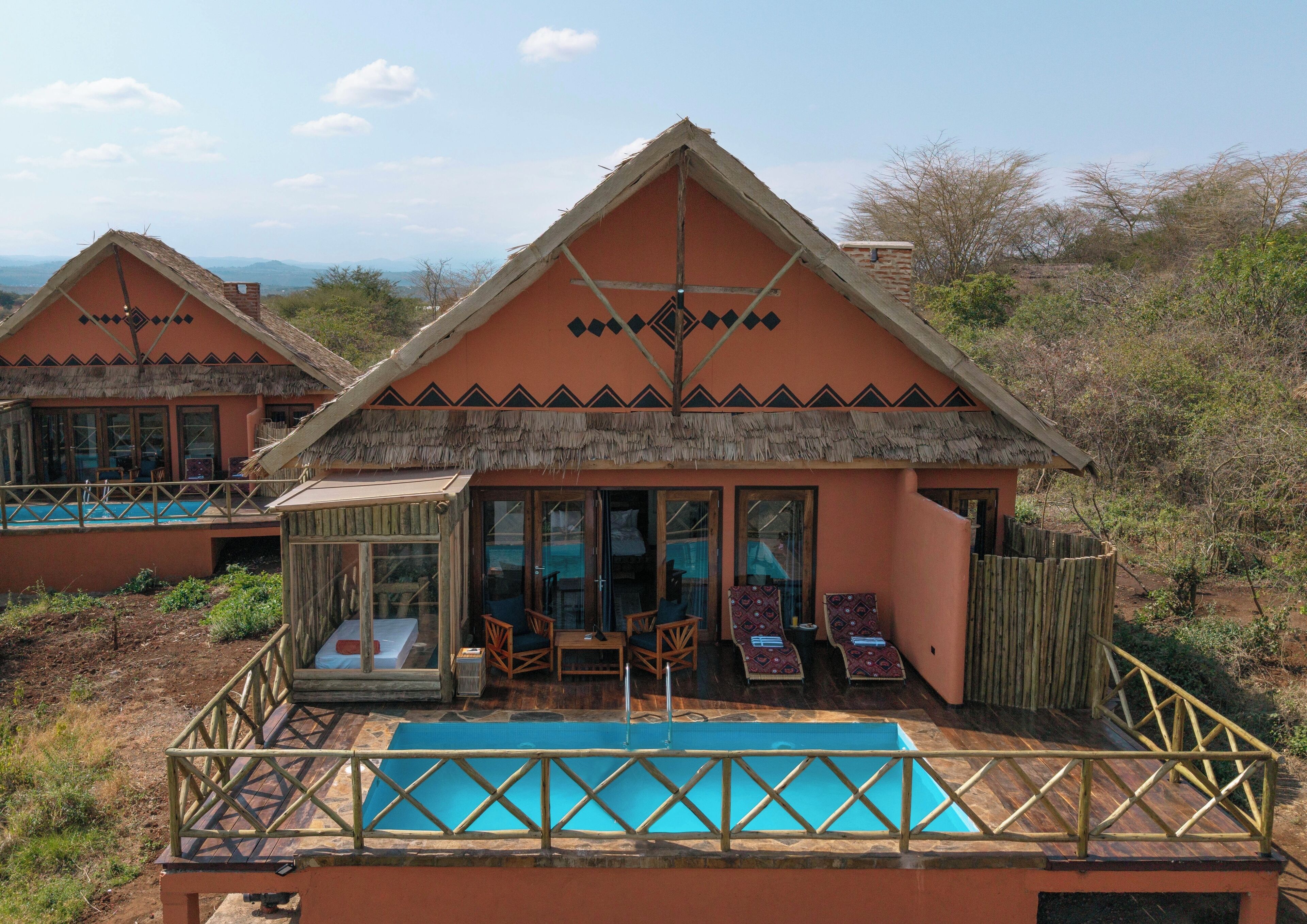 A bungalow with a pool, thatched roof, and a view of the surrounding landscape.