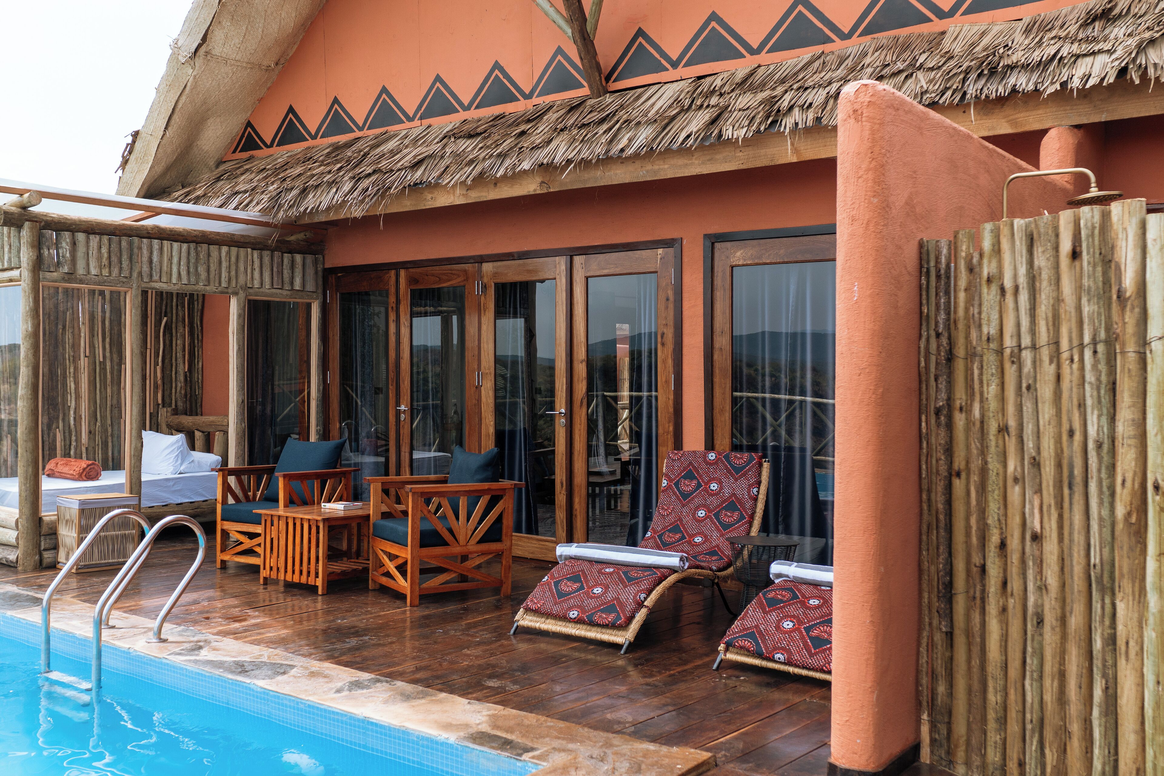 A poolside area with lounge chairs, a wooden deck, and a thatched roof structure.