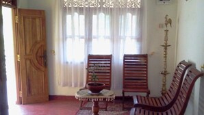 Una stanza con una porta in legno, due sedie di legno, un tavolino con una pianta e un supporto decorativo.