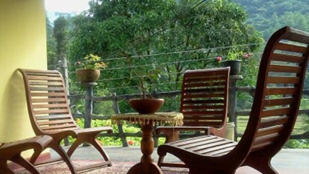 Un balcone con sedie e tavolo in legno, immerso nel verde.