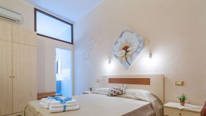 A bedroom with a large bed, a wooden wardrobe, a bedside table with a plant, and a wall-mounted artwork. - B&B Il Borgo (Cagliari)