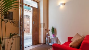 A red sofa, a wooden door, a potted plant, and a wall-mounted light fixture. - B&B Il Borgo (Cagliari)