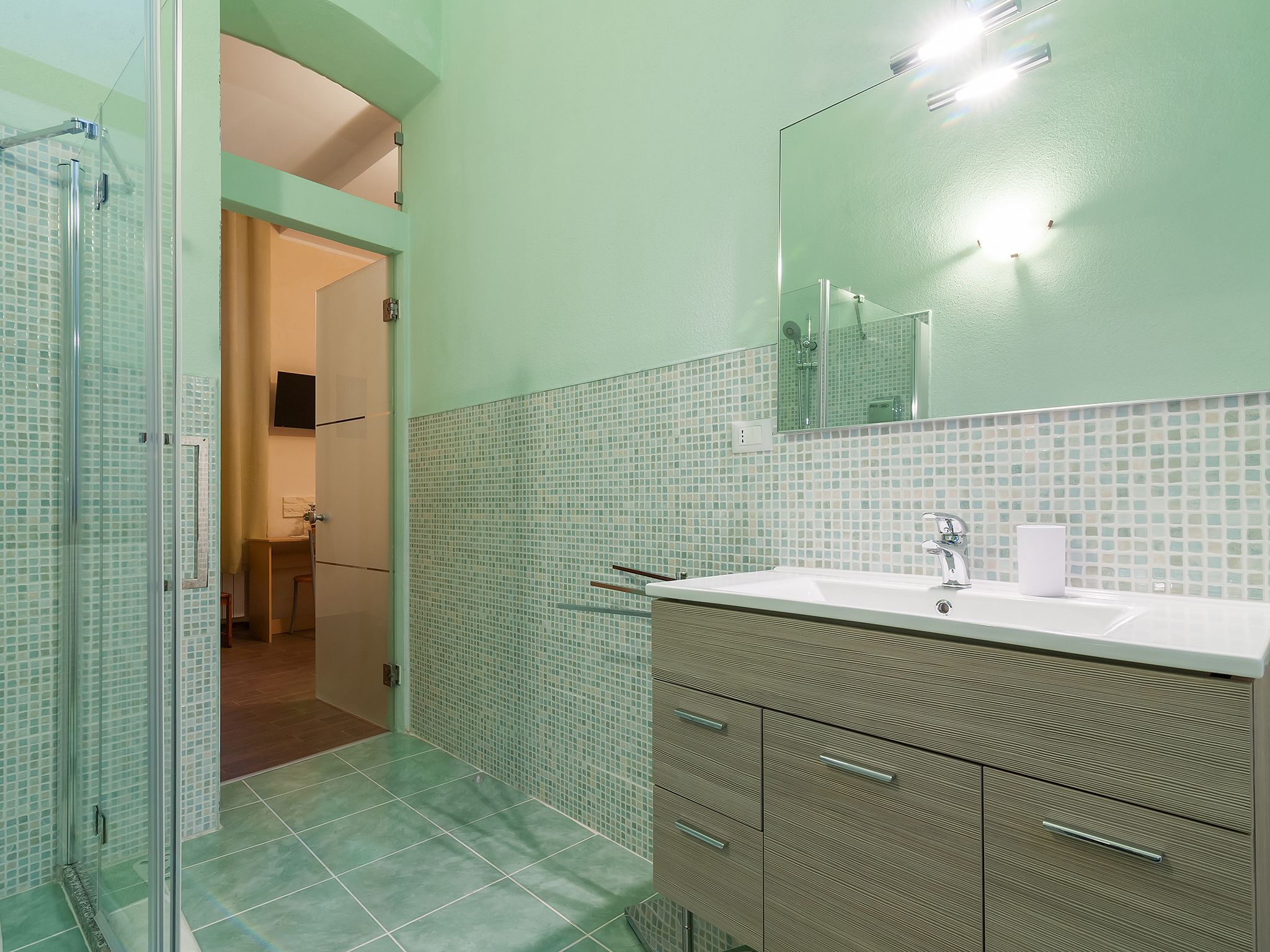 Un baño con cabina de ducha de vidrio, lavamanos con espejo y paredes con azulejos.