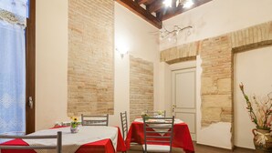 A dining area with brick walls, a wooden ceiling, and a door. Tables are covered with red tablecloths, and there are chairs around them. - B&B Il Borgo (Cagliari)