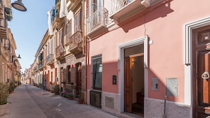 A narrow street lined with traditional buildings, featuring balconies with plants and a clear sky. - B&B Il Borgo (Cagliari)