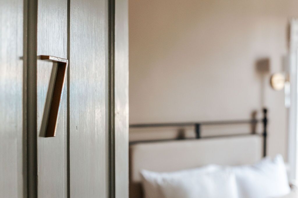 Eine Tür mit Messinggriff und ein Bett mit weißer Bettwäsche im Hintergrund.