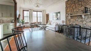 A spacious living area with a dining table, a stone fireplace, and a view of the kitchen.