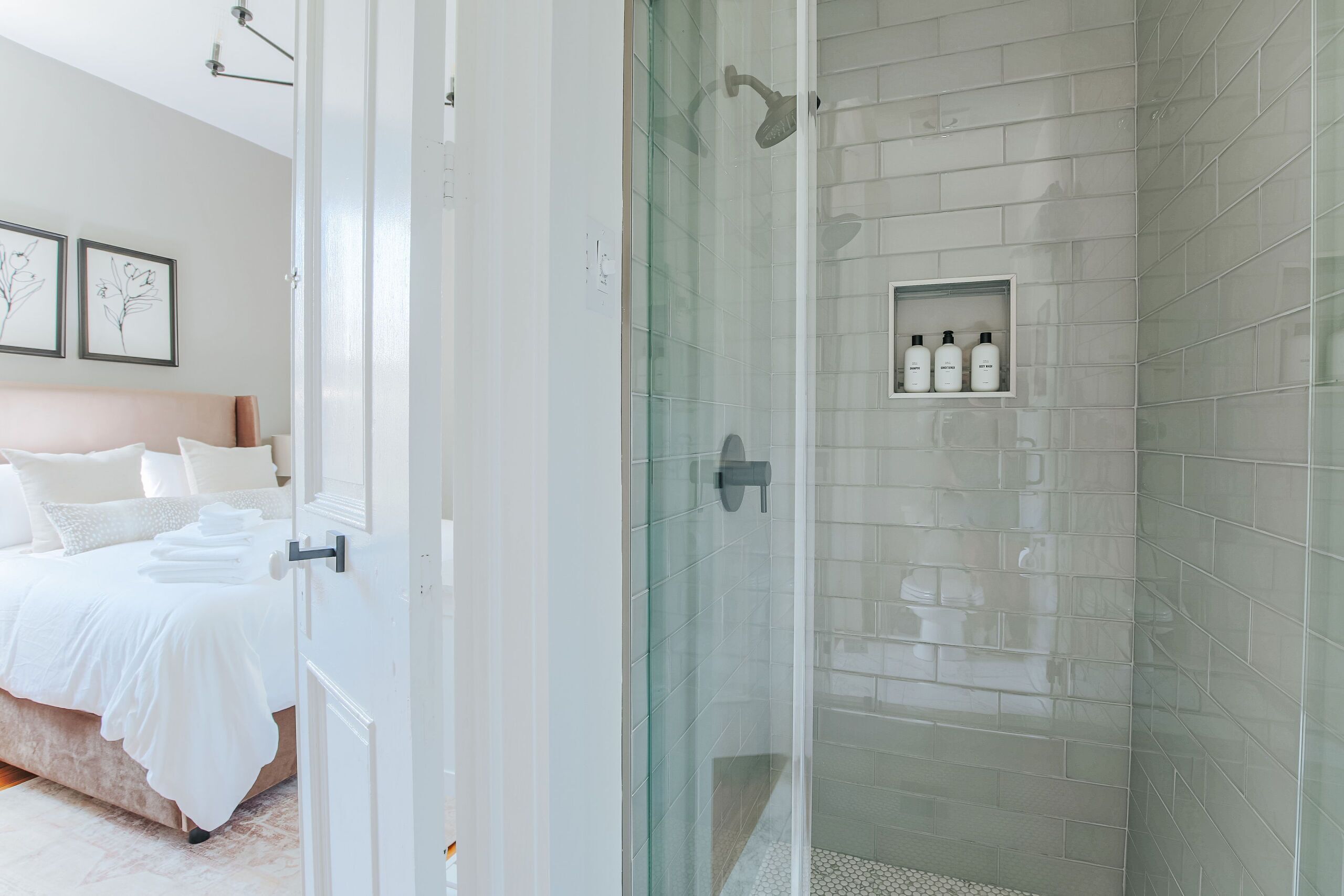 Een moderne badkamer met een glazen douchecabine, witte betegelde wanden en een plank met toiletartikelen.
