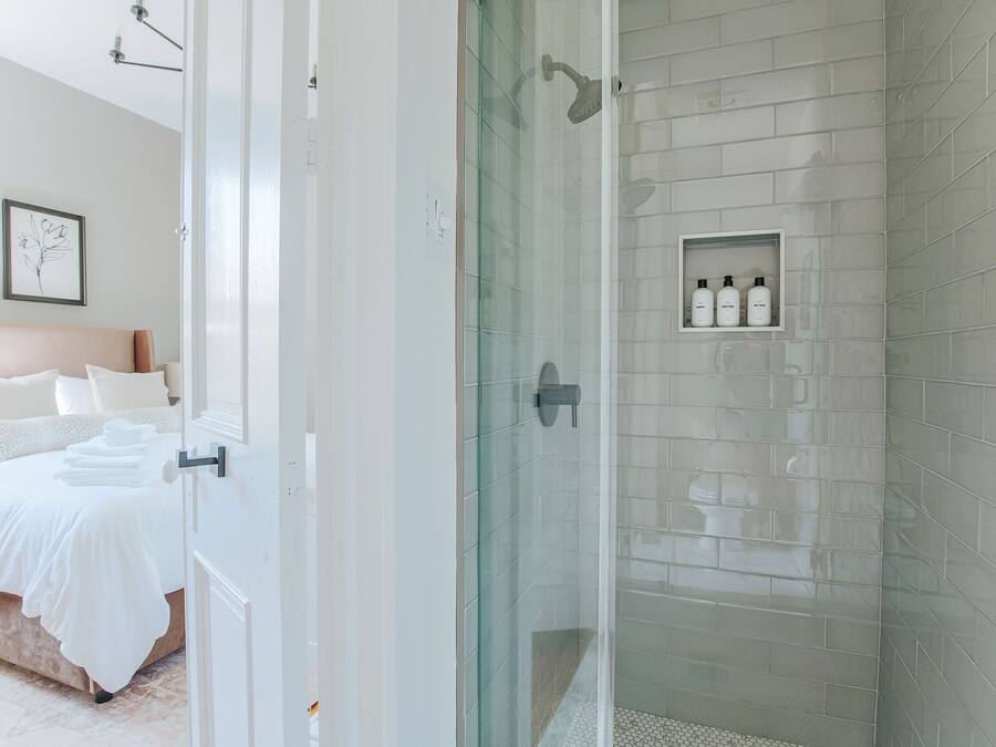 Une salle de bain moderne avec une douche à parois de verre, des murs recouverts de carreaux blancs et une étagère où sont rangés les articles de toilette.