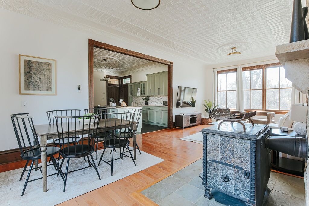 A spacious dining area with a wooden table and chairs, a stone fireplace, and a view of the kitchen through an open doorway.