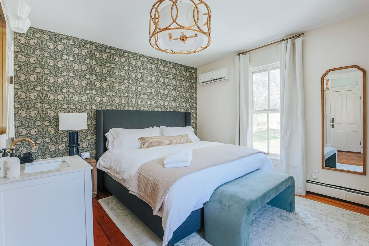 A bedroom with a bed, bedside table, lamp, and a large mirror.