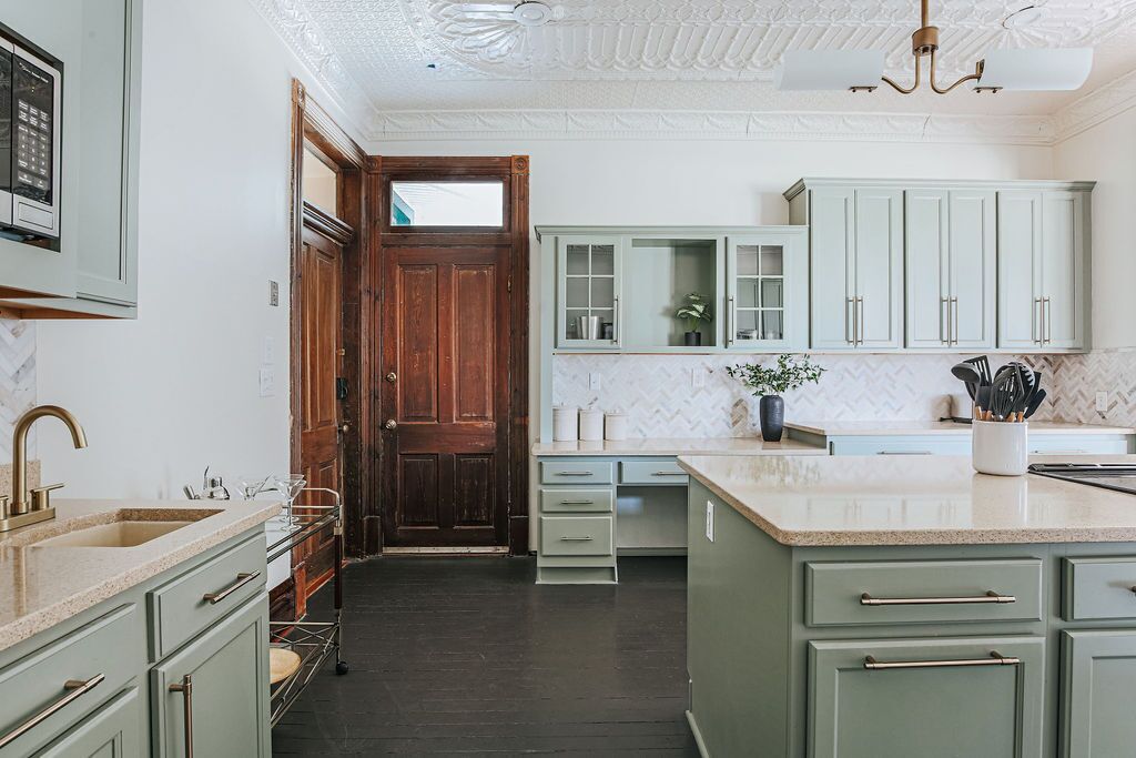Une cuisine avec des meubles de couleur vert clair, un plan de travail en marbre et une porte en bois.