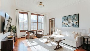 A spacious living room with a white sofa, a coffee table, and a large window with curtains.