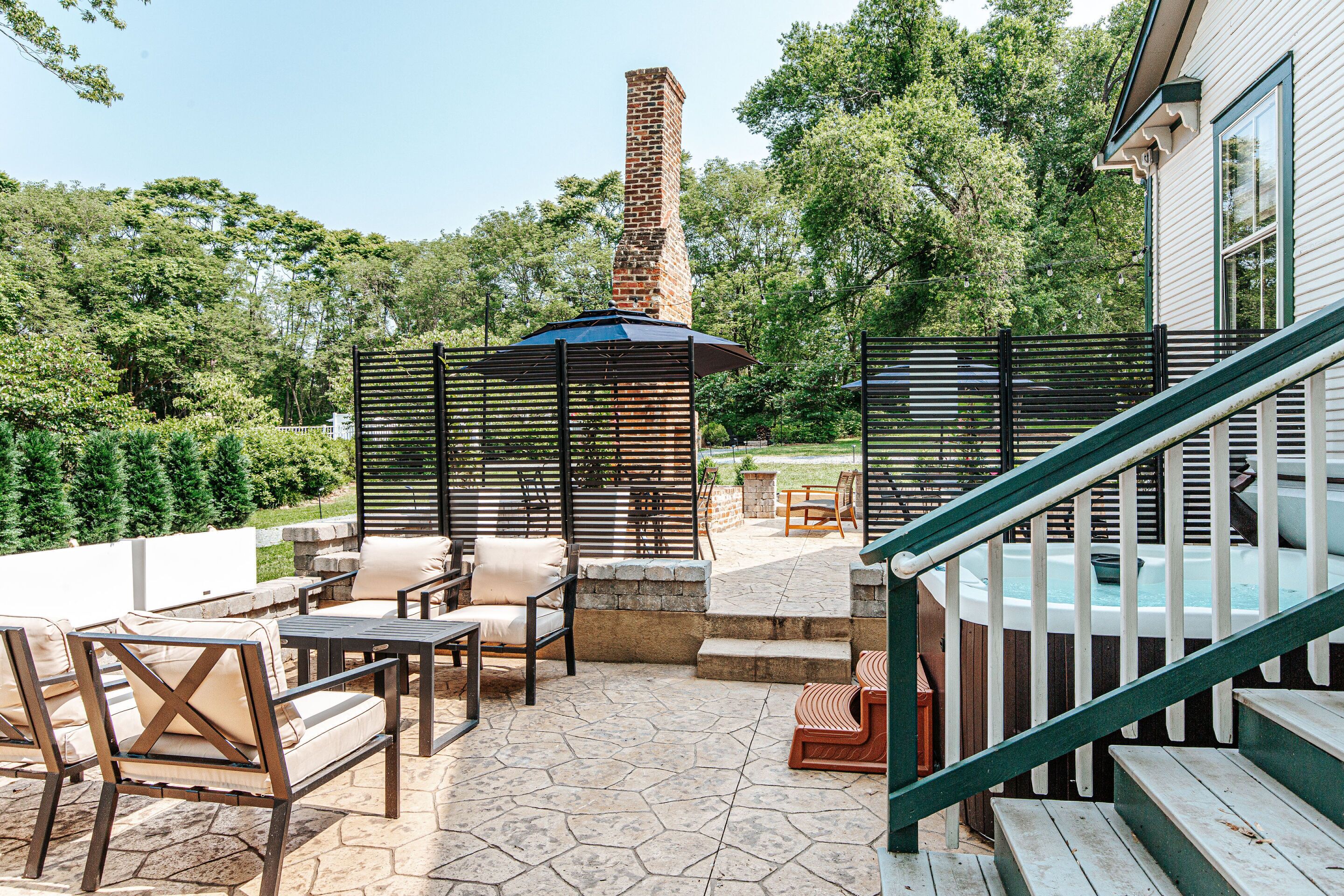 An outdoor patio area with stone flooring, outdoor furniture, a hot tub, and a brick chimney.