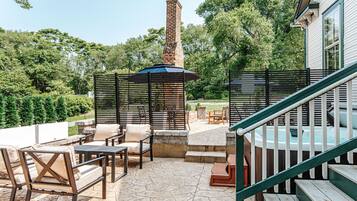 An outdoor patio area with stone flooring, outdoor furniture, a hot tub, and a brick chimney.