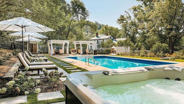 A backyard with a swimming pool, lounge chairs, and umbrellas.