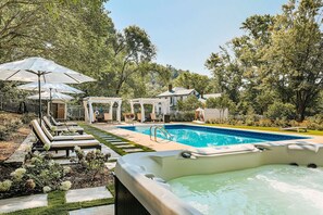 Un patio trasero con piscina, sillas de descanso y sombrillas.