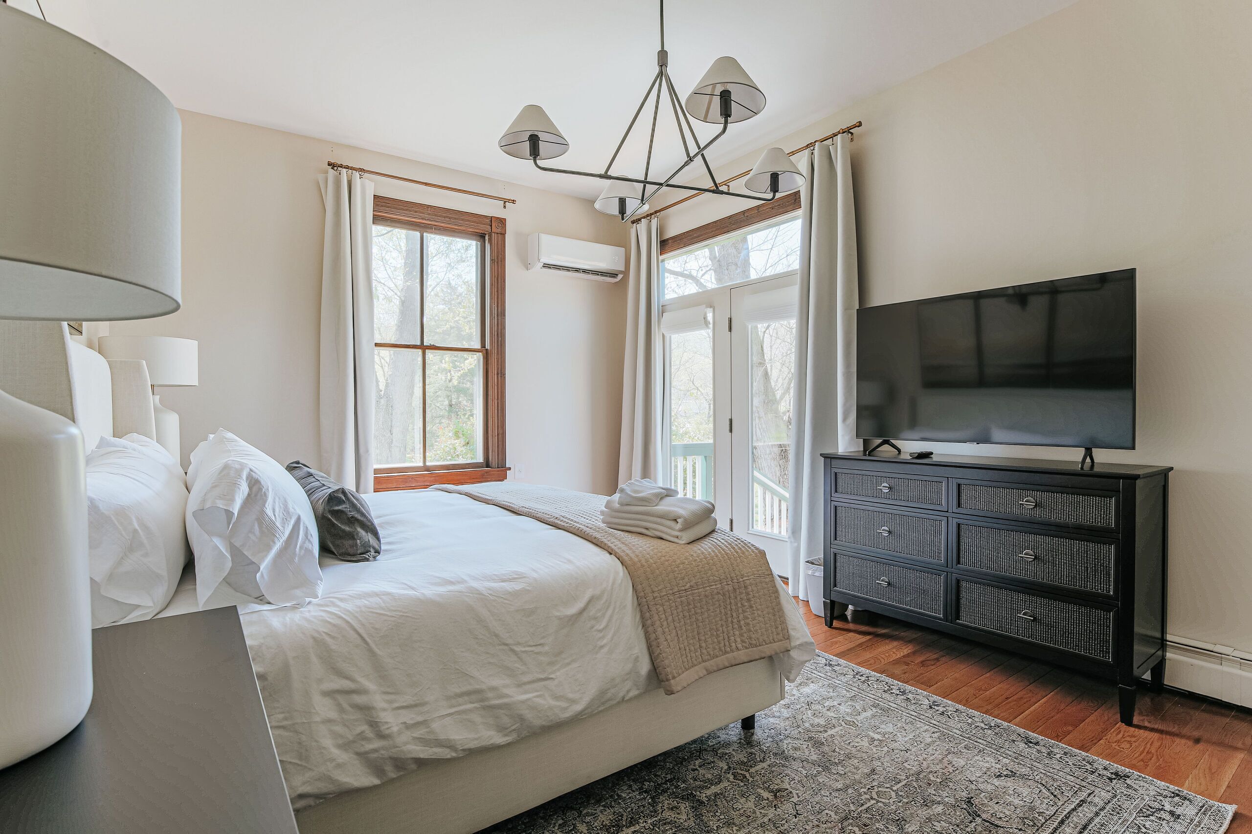 A bedroom with a bed, a dresser, a television, and a window with curtains.