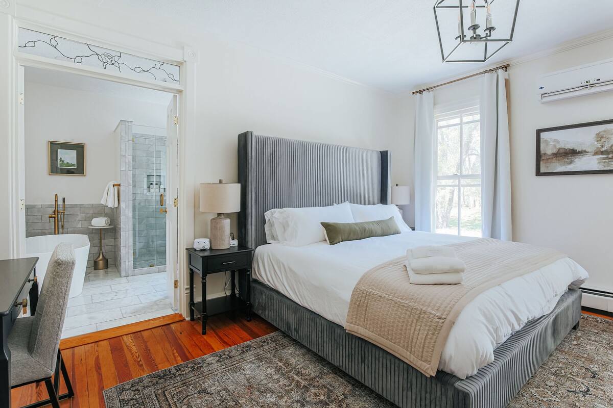 A bedroom with a large bed, bedside tables, a desk, and a shower area.