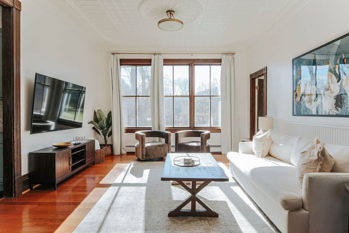 A spacious living room with a large TV, two armchairs, a sofa, and a coffee table.