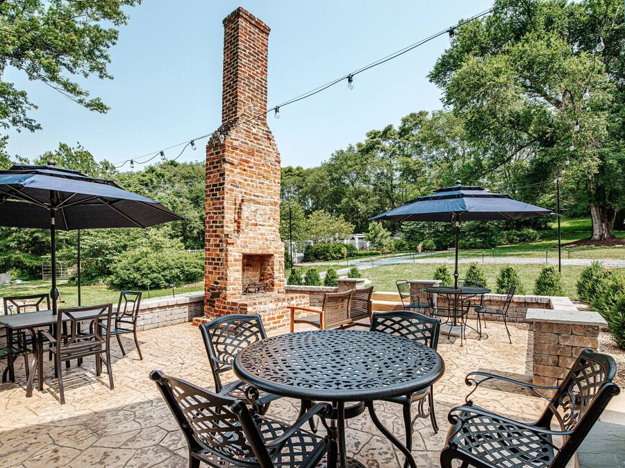 An outdoor patio with brick barbecue grill, tables, chairs, and umbrellas.