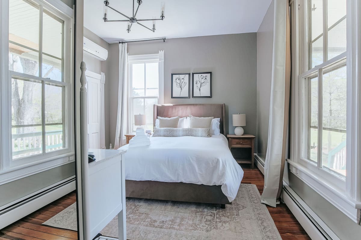 A bedroom with a large bed, bedside tables, a chandelier, and large windows.