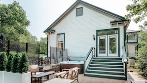 A house with a patio area featuring outdoor furniture, a hot tub, and a staircase leading to the front door.