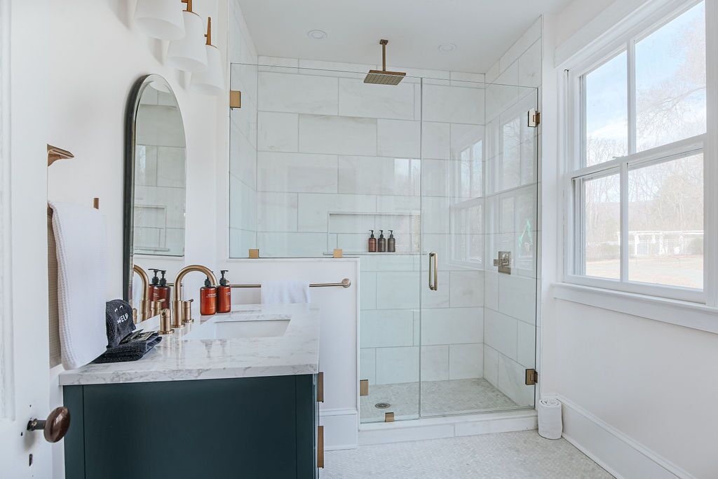 A modern bathroom with a large mirror, two sinks, a shower, and a window.