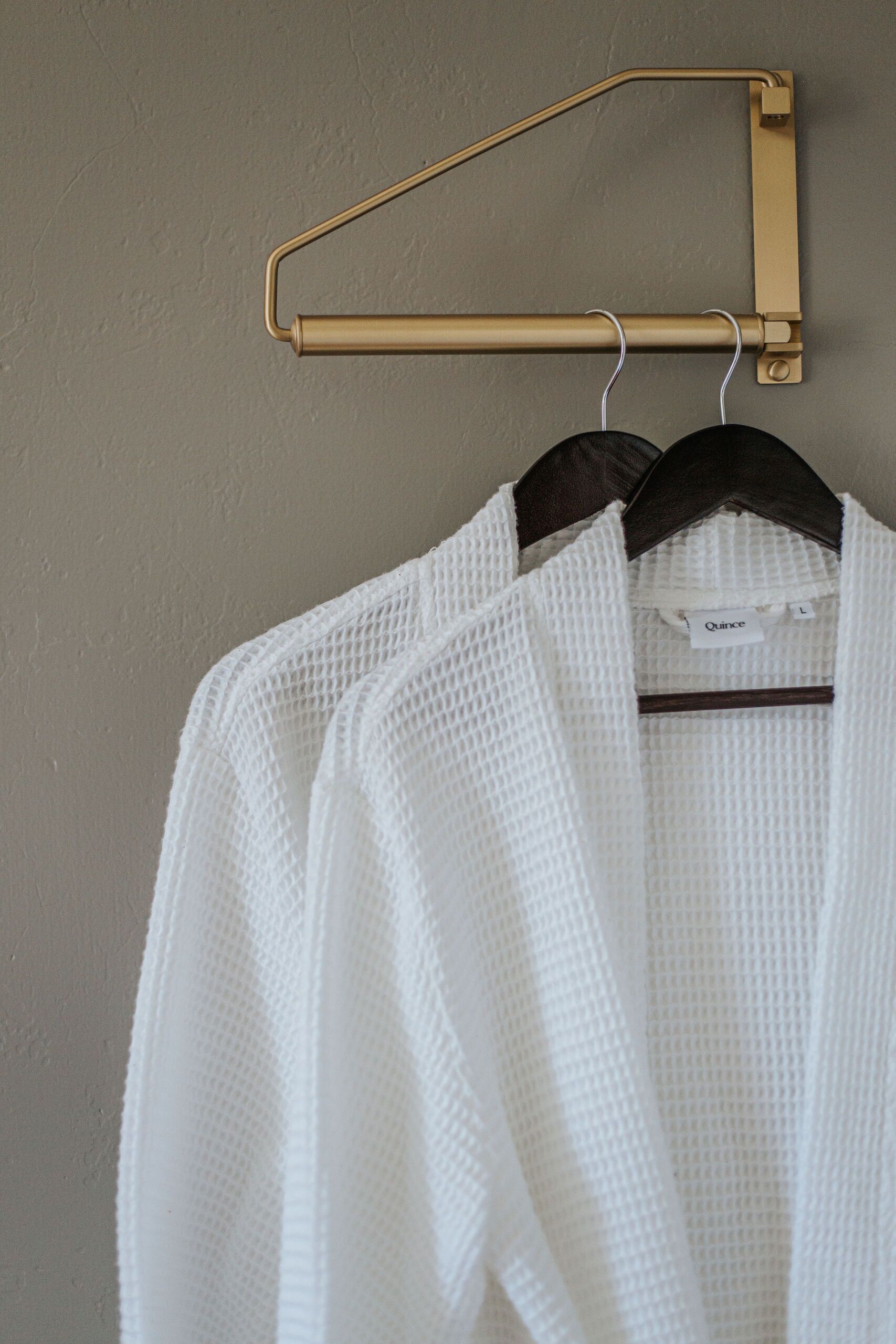 A white knitted sweater hanging on a gold-colored hanger against a textured wall.
