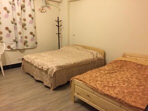 Ein Schlafzimmer mit zwei Einzelbetten, einem Holzstuhl, einem Kleiderständer und einem Vorhang mit Blattmuster.