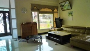 A living room with a sofa, coffee table, and a small round table. There is a window with a view outside, a clock on the wall, and a door leading to another room. - Wish Enjoy Happy Homestay (Ligang)