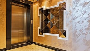 Um elevador moderno com acabamento metálico e um painel decorativo na parede com padrões geométricos.