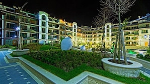 Um hotel moderno com vários andares, iluminação externa e jardins ajardinados.